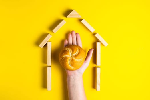 Hand holding money coins close to bread on a yellow background