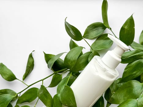 Close up of white lotion bottle surrounded by green leaves on white background. Skincare and natural beauty concept. Design for healthcare, wellness, and organic product poster. High quality photo