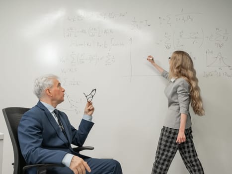 Female student answers a question from an elderly professor at a white board