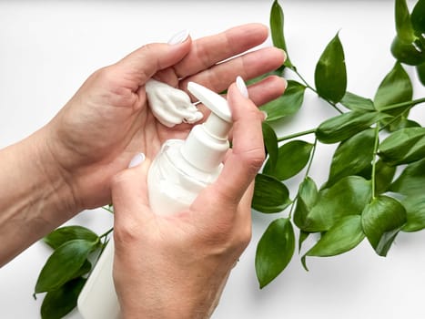 Close up of middle age woman hands dispensing lotion from bottle with green leaves on white background. Skincare and natural beauty concept. For healthcare, wellness, and organic product poster.