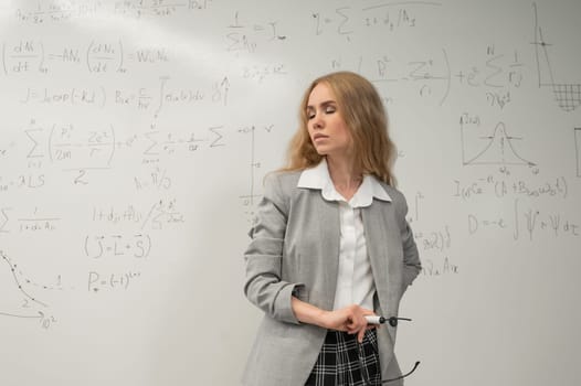 A Caucasian woman stands at a blackboard with written formulas