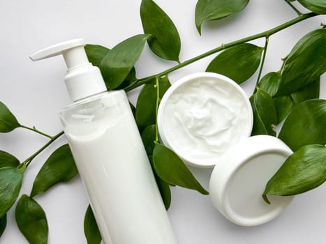 Close up of white lotion bottle and hand cream container with green leaves on white background. Skincare and natural beauty concept. For healthcare, wellness, and organic product poster. High quality