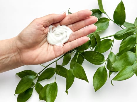 Close up of middle age woman hand holding of hand cream with green leaves on a white background. Skincare and natural beauty concept. For healthcare, wellness, and organic product poster. High quality