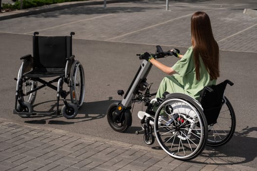 Woman in wheelchair with assistive device for manual control next to classic wheelchair. Electric handbike