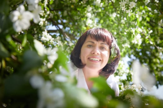 Girl walking, Relaxing near Blossoming apple Tree on Sunny Day. Portrait of Middle aged woman enjoying nature surrounded by white blossoms