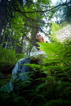 Adult mature woman 40-60 in a green long fairy dress in forest. Photo shoot in style of dryad and queen of nature. Fairy in beautiful green summer forest. Concept of caring for nature