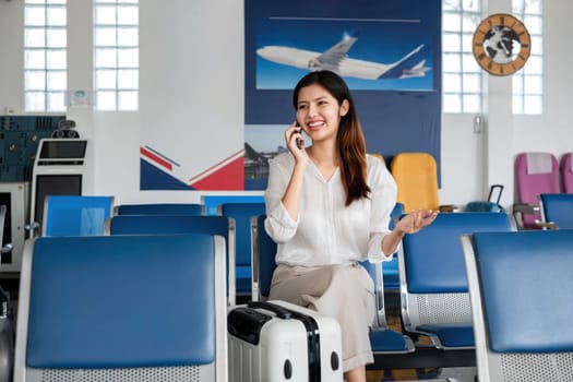 Asian woman using smartphone in airport waiting area for travel. Concept of communication, travel, and modern transportation.