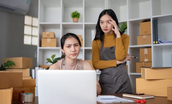 Two young Asian women who are worried Was stressed while running a small business together having trouble selling products online using a laptop..