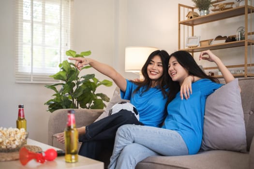 A lesbian couple cheers football and celebrate together for their favorite Euro football team. A young female couple cheers football on TV together in the living room on match day..