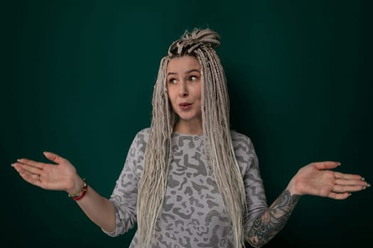 A woman with dreadlocks is standing against a solid green background. She is looking directly at the camera, with a confident expression on her face.