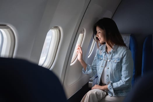 Asian woman looking out airplane window during flight. Concept of travel, aviation, and contemplation.