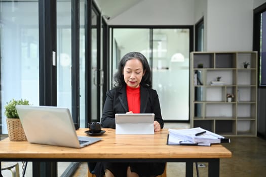 Portrait of elegant mature businesswoman using digital tablet at her workplace.