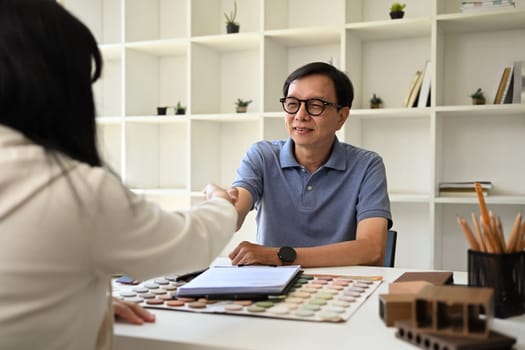 Smiling senior male interior designer shaking hands with his client after signing contract at office.