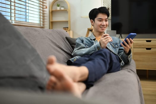 Relaxed young man with credit card in hand and using smartphone for shopping online.