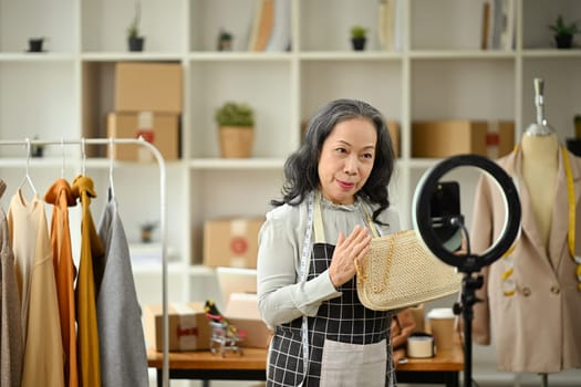 Confident senior business owner live streaming to sale clothes product to customers at her clothing shop.