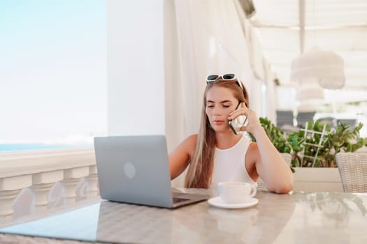 Woman coffee cafe laptop. Coffee break in cafe with sea view. Tranquil long haired woman drinking coffee in plant filled place. Woman sitting at a coffee shop with mobile phone drinking coffee