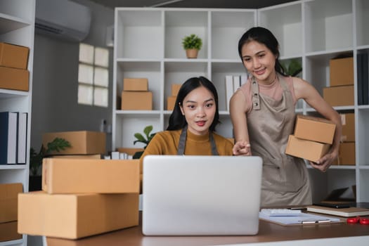 Two women working on laptop and packing boxes in warehouse.