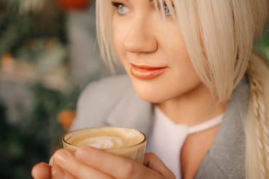 A blonde woman is holding a cup of coffee. She is wearing a gray jacket and white shirt