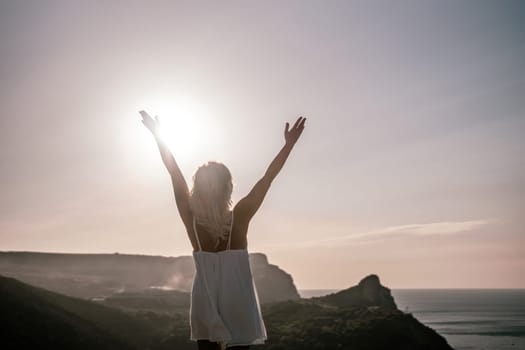 A woman is standing on a hill overlooking a body of water. She is wearing a white dress and she is happy