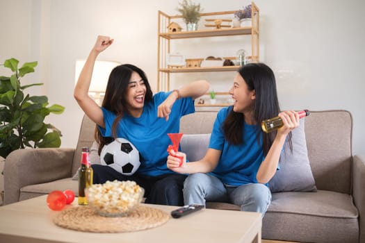 A lesbian couple cheers football and celebrate together for their favorite Euro football team. A young female couple cheers football on TV together in the living room on match day..