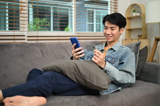 Happy young Asian man holding credit card making payment on mobile phone. Internet banking and e-commerce concept.