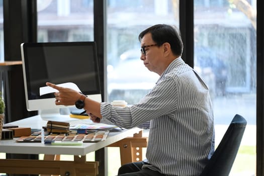 Senior male interior designer choosing materials and color for indoor decor project at office.