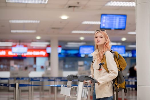 Young traveler with luggage cart and backpack at airport terminal. Concept of travel, exploration, and excitement.