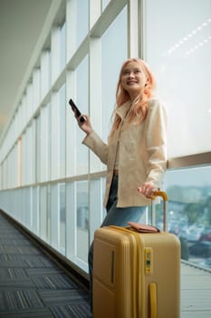 Asian woman talking on smartphone with luggage in airport terminal. Concept of travel, communication, and anticipation.