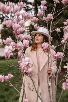 Woman magnolia flowers, surrounded by blossoming trees, hair down, white hat, wearing a light coat. Captured during spring, showcasing natural beauty and seasonal change