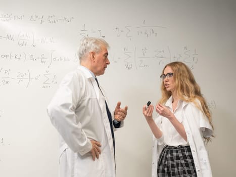 An elderly man and a young woman at a white board. Colleagues scientists discuss work issues