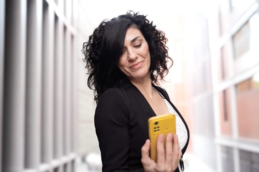 Young woman with cell phone in hands, writes messages and reads news online, using an app with a gesture of happiness.