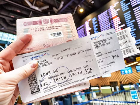 Moscow, Russia - April 04, 2024: Passport and air ticket in hand and the departure board at the airport in the background. Concept of travel in Russia