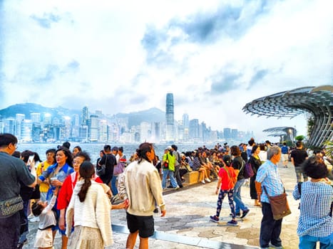 Hong Kong - April 05, 2024: People gather on the Hong Kong waterfront, with skyscrapers and Victoria Bay in the background on a cloudy afternoon