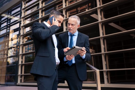 Two trusted business colleagues dressed in formal attire with a digital tablet in hand observing the results of the work done