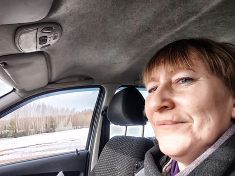 Funny Middle aged woman in car taking selfie while enjoying a drive. Female mature driver posing inside car. Funny happy tourist girl in alone travel