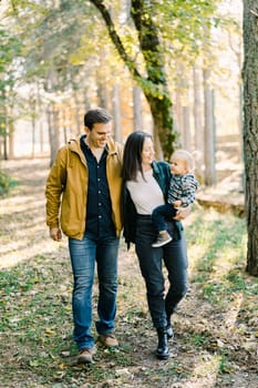 Smiling dad and mom with a little daughter in her arms walk through the park. High quality photo