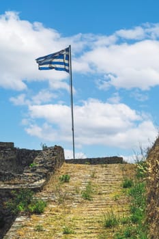 Greek flag waving on a must against sky with clouds on top of Agia Mavra Fort in Lefkada Ionian Island, Greece.