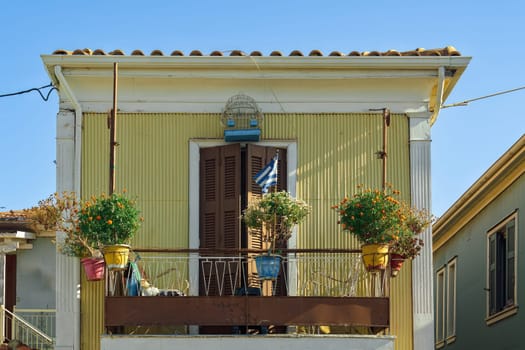 Old colorful house face with flowers on an iron balcony and Greek flag waving in Lefkada Ionian Island Greece.