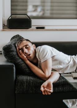 One young Caucasian handsome guy sleeps soundly with his mouth open while lying on the sofa in the salon on a summer day, close-up side view in slow motion.