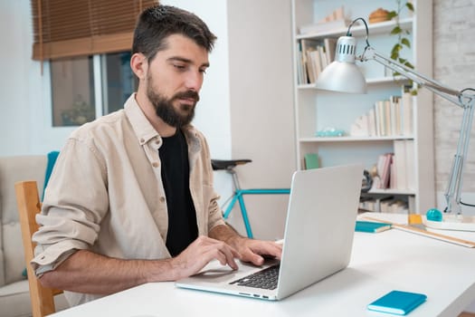 Business man working on laptop at home office. Young student or remote teacher using computer remote studying, virtual training, watching online education webinar at home office. High quality photo