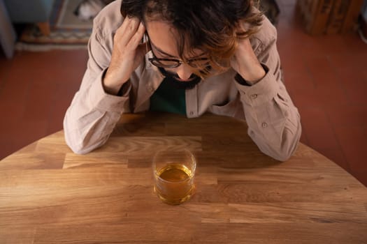 Upset young man drinker alcoholic sitting at bar counter with glass drinking whiskey alone, sad depressed addicted drunk guy having problem suffer from alcohol addiction abuse, alcoholism concept. High quality photo