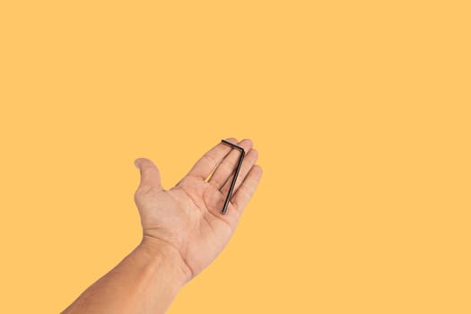 Black male hand holding an allen key isolated on yellow background. High quality photo