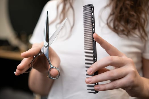 Female hairdresser holding scissors and comb in her hands.