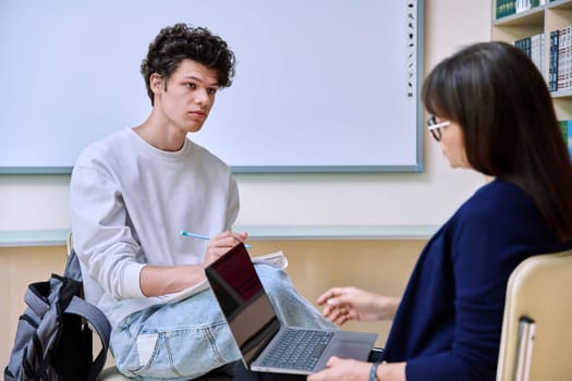 Guy college student talking studying with female teacher. Mentor and student together in the classroom. Education, training, mentoring, teaching, youth concept