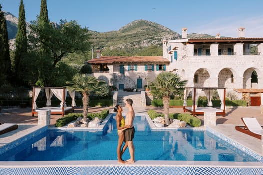 Man and woman stand hugging and looking at each other on the edge of a swimming pool near an old villa. High quality photo