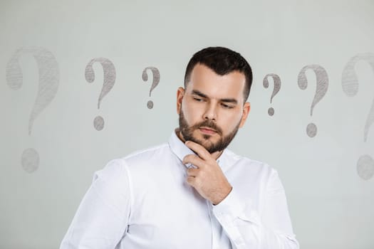 portrait of doubtful bearded man in white shirt asking questions on gray background.