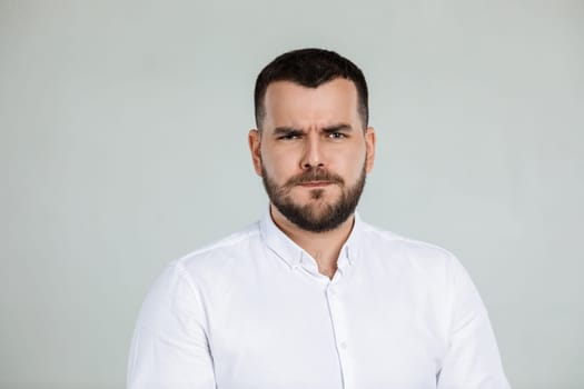 Portrait of young frowned handsome bearded man on gray background. facial expression