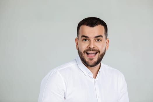 Portrait of young surprised handsome bearded man with shocked facial expression on gray background