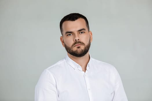 portrait of sad bearded man in white shirt on gray background