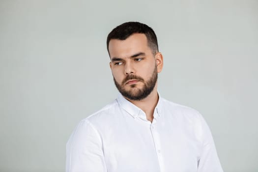 portrait of sad bearded man in white shirt on gray background